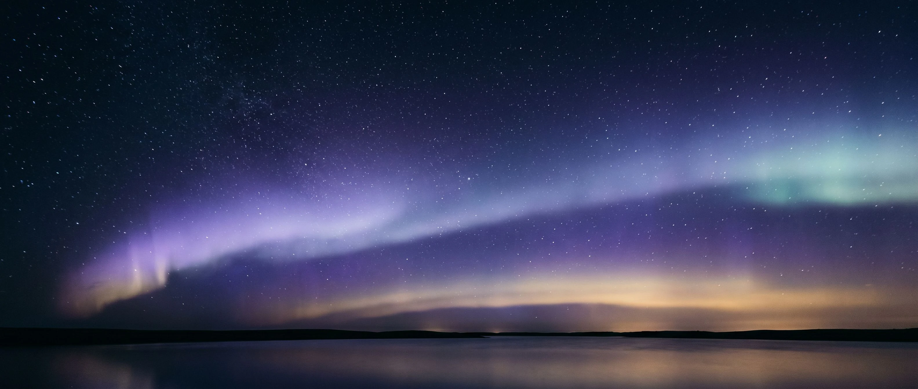 Ночное звёздное небо с мягким aurora-свечением над тёмным горизонтом. Атмосферный пейзаж в тонах индиго, лаванды и слабого золота.